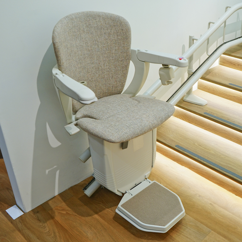 A modern upholstered stairlift beside a wooden staircase with soft step lighting